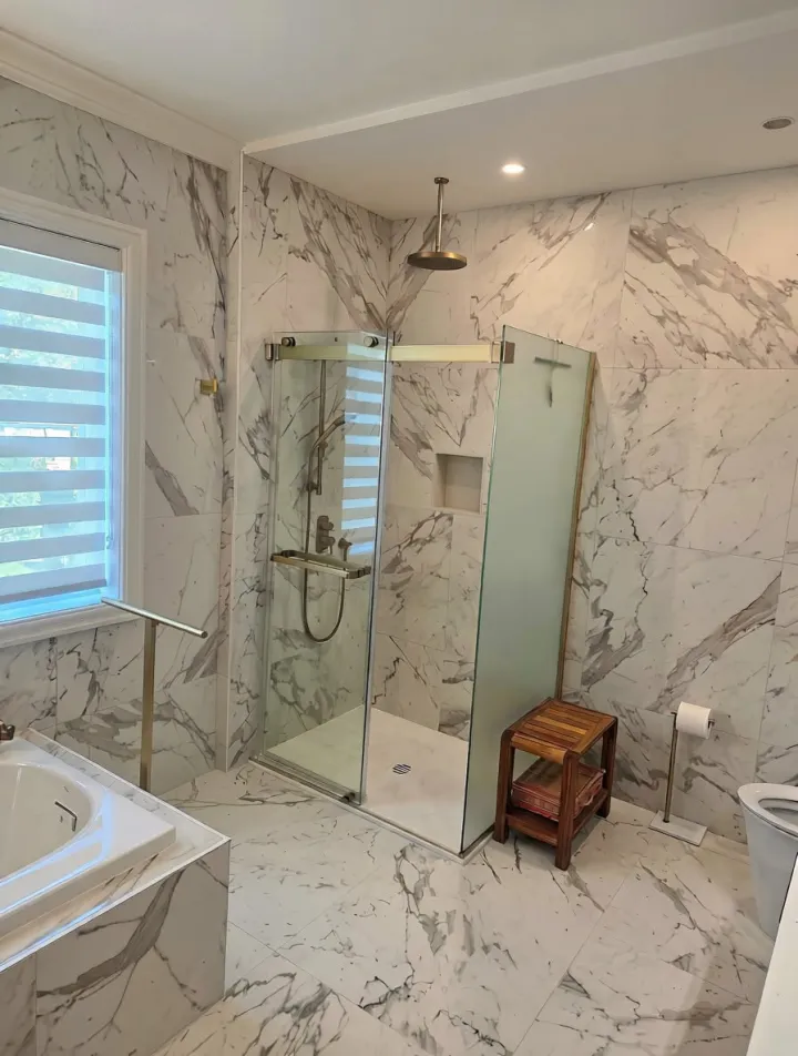 Salle de bain rénovée avec douche vitrée et revêtement effet marbre