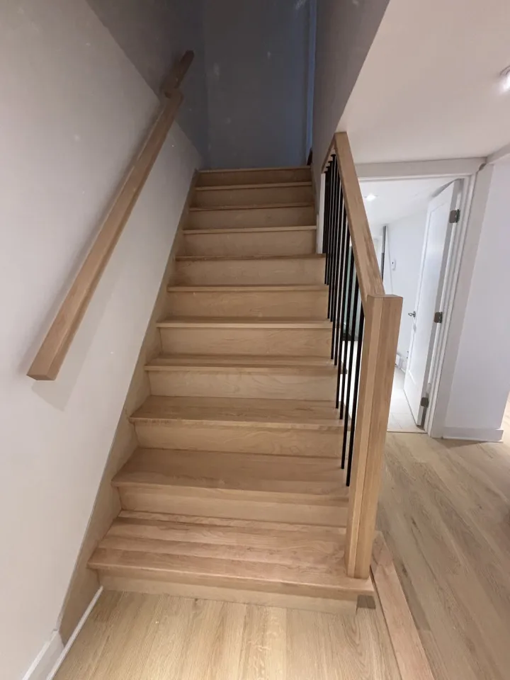 Escalier en bois clair avec garde-corps noir dans une rénovation intérieure
